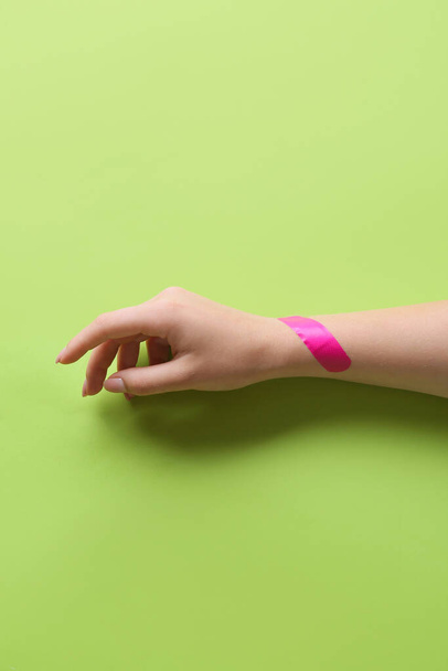 Female hand with medical plaster on green background - 写真・画像