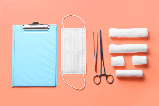 Klemmbrett, medizinische Maske, chirurgische Werkzeuge und Verbandsrollen auf farbigem Hintergrund - Foto, Bild