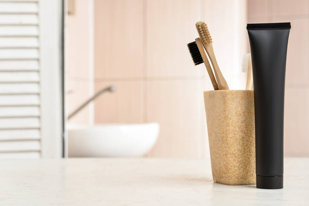 Černá zubní pasta s aktivním uhlím a kartáčky na stole v koupelně - Fotografie, Obrázek