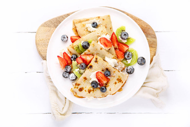 Sweet crepes with berries and cream on white wooden background. Homemade food concept. Top view, flat lay, copy space - Fotografie, Obrázek