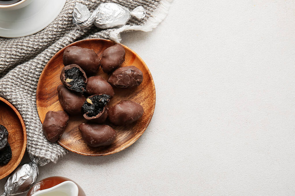 Delicious chocolate candies with prunes in wooden plate on light table - Fotó, kép