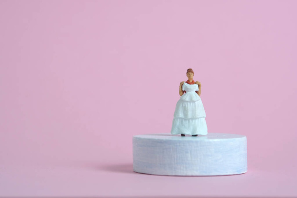 Nők miniatűr emberek próbálnak választani esküvői ruha felett álló platform talapzat kék rózsaszín háttér. Képfotó - Fotó, kép