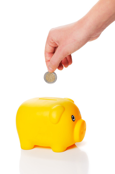 żółty piggy bank się monety 2 euro od ręki - Zdjęcie, obraz