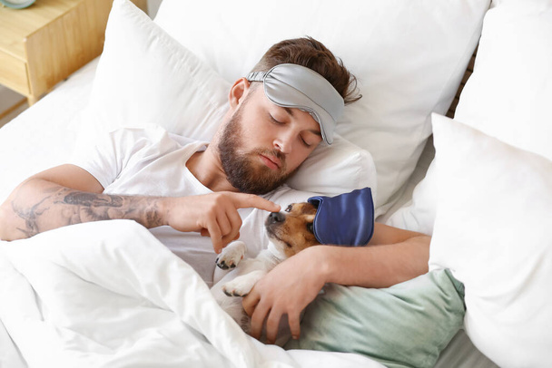 Young man with sleeping mask and cute dog lying in bed - Photo, Image