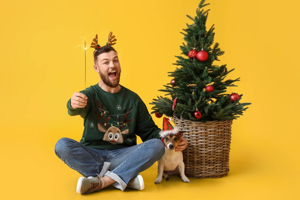 Young man with Christmas sparkler and cute dog on yellow background - Foto, Imagem