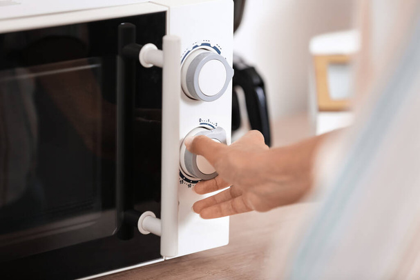Young woman adjusting microwave oven in kitchen, closeup - 写真・画像