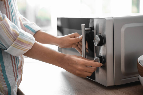 Young woman adjusting microwave oven in kitchen, closeup - Foto, Imagen