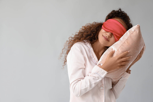 Junge Afroamerikanerin mit Schlafmaske und Kopfkissen auf grauem Hintergrund - Foto, Bild