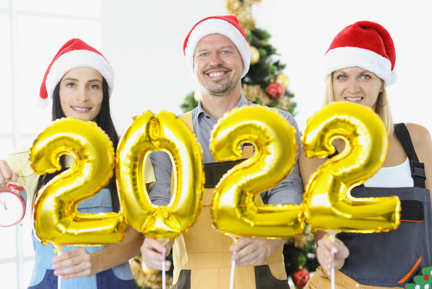 Altın helyum balonları tutan bir grup tamirci. Yeni yıl ağacına yakın 2022 numara. - Fotoğraf, Görsel