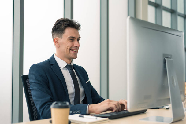 Der erwachsene smarte Geschäftsmann im Anzug sitzt und arbeitet im modernen Büro vor der Computertastatur - Foto, Bild