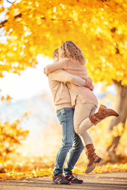 Ένας άντρας κρατά στην αγκαλιά του μια γυναίκα σε μια αγκαλιά με φιλιά στο πάρκο του φθινοπώρου. - Φωτογραφία, εικόνα