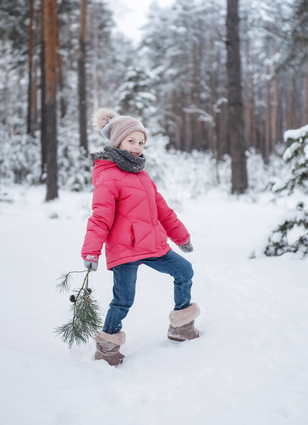 Mała dziewczynka w jasnej kurtce bawi się w zimowym śnieżnym lesie. - Zdjęcie, obraz