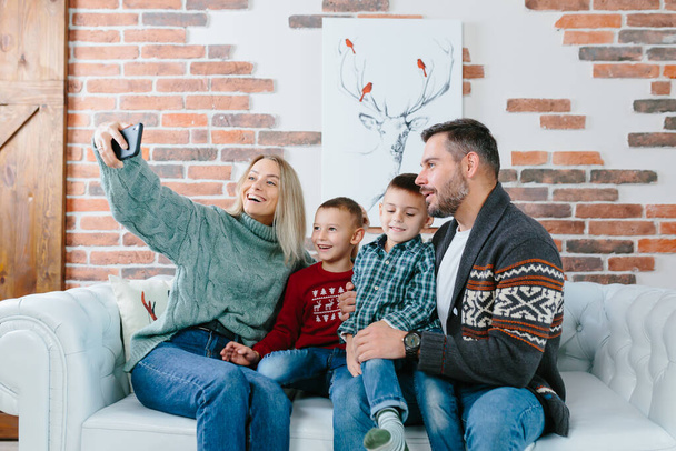 Young family having fun talking on a video call using a mobile phone, rejoicing and smiling, husband wife and your guys brothers greet friends with New Year and Christmas holidays - Zdjęcie, obraz