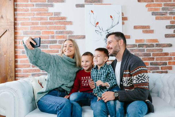 Young family having fun talking on a video call using a mobile phone, rejoicing and smiling, husband wife and your guys brothers greet friends with New Year and Christmas holidays - Fotografie, Obrázek