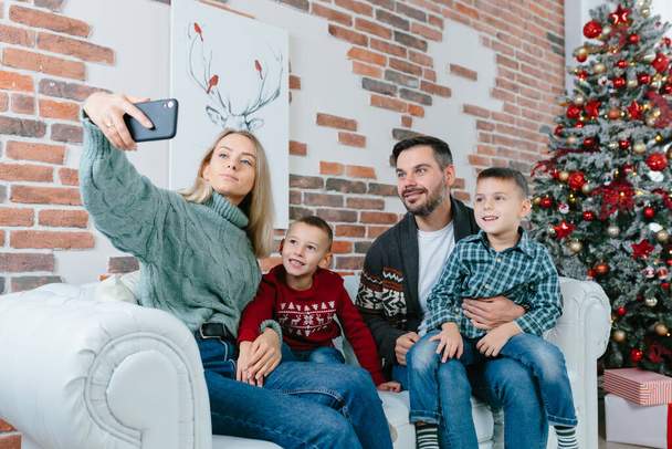 Beautiful happy married couple with two children using smart phone talking to friends or family congratulates Merry Christmas by video call conference app. Modern technology New Year 2022 congrats. - Fotó, kép