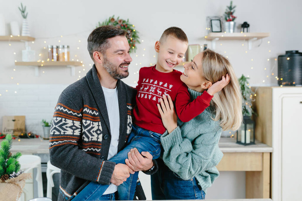 A young family with a son in the kitchen rejoice in the holidays, a husband and wife and a little boy have fun together hugging and playing on New Year's and Christmas holidays - Foto, Imagem