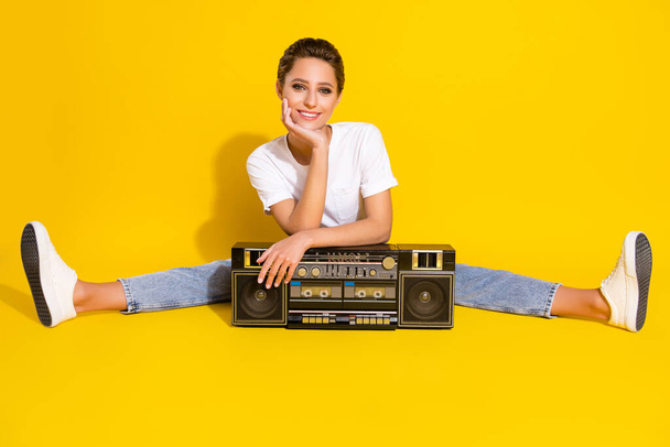Photo of charming dreamy young lady wear casual clothes sitting floor listening boom box smiling isolated yellow color background - Foto, immagini