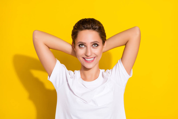 Photo of charming sweet young woman dressed casual outfit smiling arms behind head looking empty space isolated yellow color background - Foto, Bild