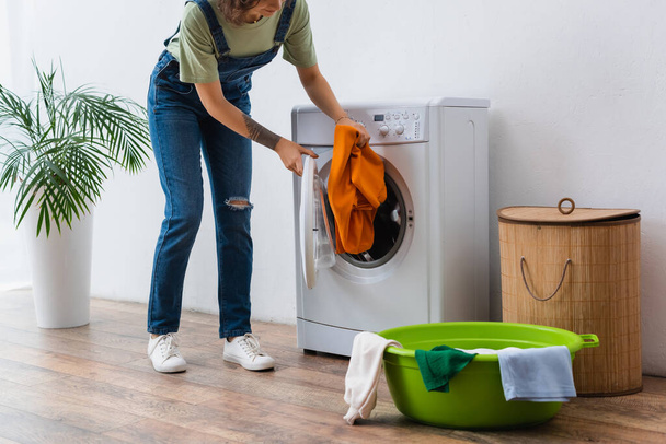 cropped view of housewife putting clothes into washing machine near laundry bowl and basket - Foto, imagen