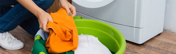 partial view of woman holding clothing near laundry bowl and washing machine, banner - Фото, изображение