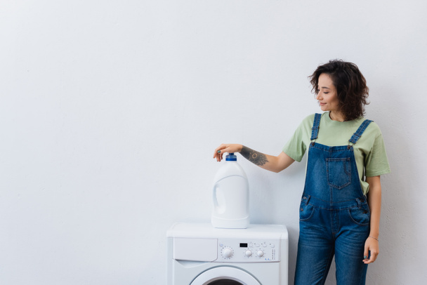 smiling housewife standing near bottle of detergent on washing machine - 写真・画像