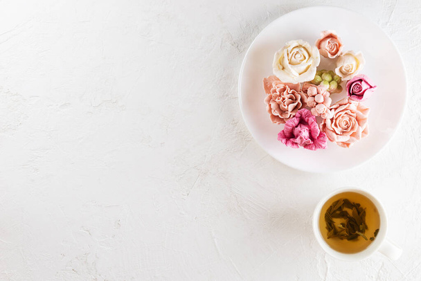Finom virágok mályvacukorból egy tányéron egy csésze zöld teával. Vízszintes tájolás, felülnézet, másolás. - Fotó, kép