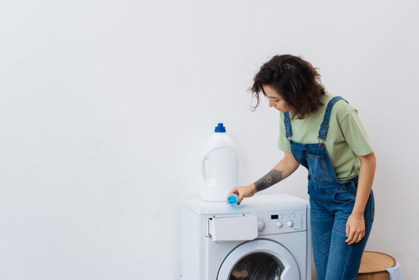 morena mujer añadiendo detergente líquido en la lavadora - Foto, Imagen