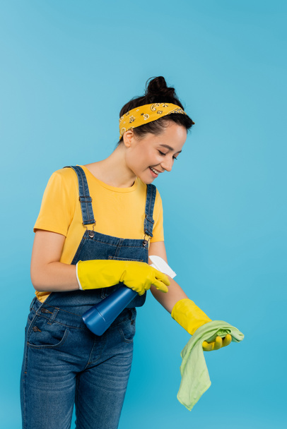 smiling housewife spraying detergent on rag isolated on blue - Foto, Imagem
