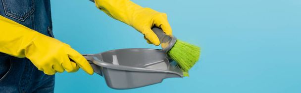 cropped view of woman in yellow rubber gloves holding scoop and broom isolated on blue, banner - Photo, Image