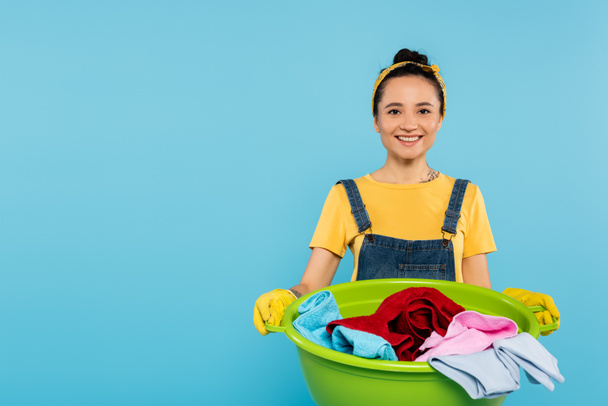 stylish and cheerful woman with laundry bowl smiling at camera isolated on blue - Zdjęcie, obraz