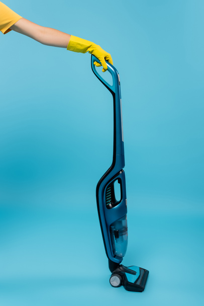 cropped view of housewife in yellow rubber glove holding modern vacuum cleaner on blue - Photo, Image