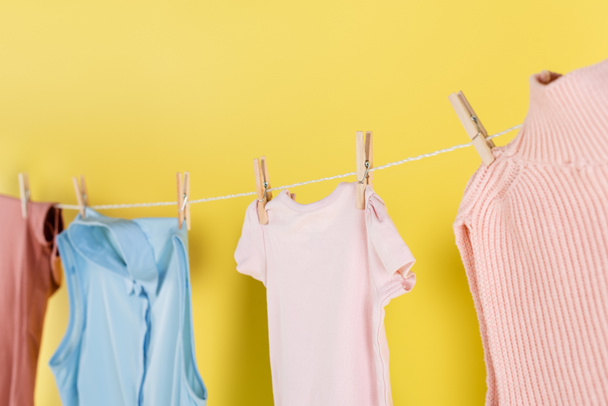 blurred laundry hanging on rope with clothes pins on yellow background - Fotografie, Obrázek