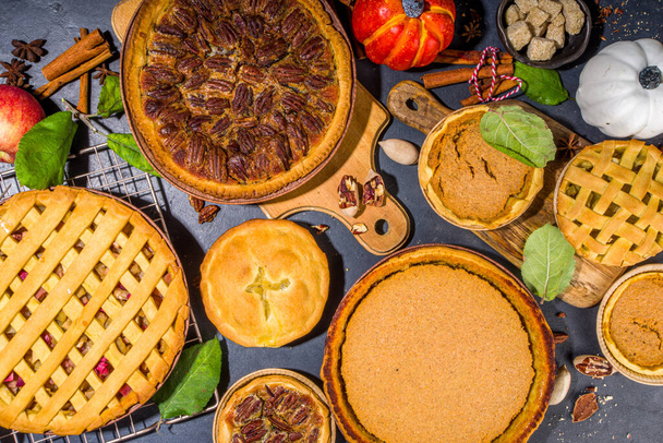 Set variety autumn pies. Pecan, apple, pumpkin small tart cakes and pies on concrete background with bright sun light, dark shadows top view  - Photo, Image