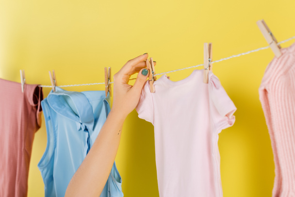 bijgesneden weergave van huisvrouw opknoping kleding op touw op gele achtergrond - Foto, afbeelding