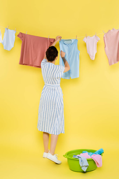 back view of housewife hanging clothes on rope on yellow background - Foto, immagini