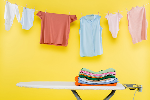 clean clothes hanging on rope over ironing board on yellow background - Zdjęcie, obraz