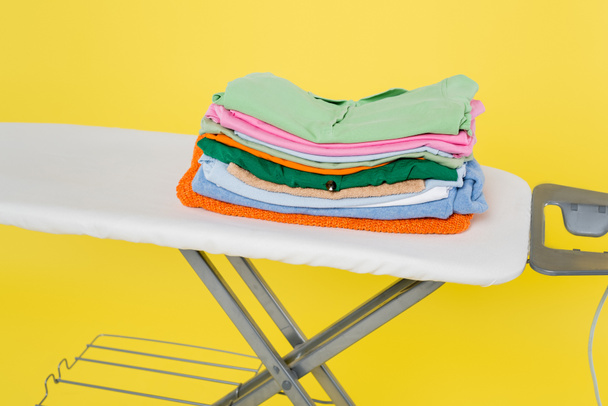 στοίβα από καθαρά ρούχα σε σιδερώστρα που απομονώνονται σε κίτρινο - Φωτογραφία, εικόνα