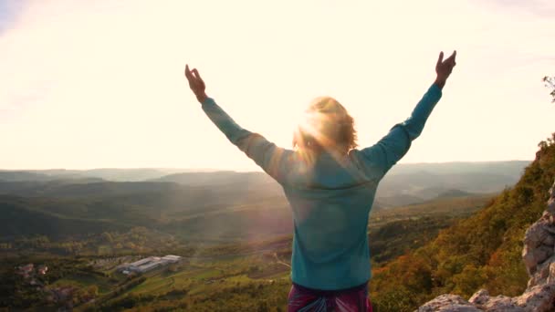 Νεαρή κοπέλα σήκωσε τα χέρια της στον ήλιο με φόντο τα βουνά - Πλάνα, βίντεο