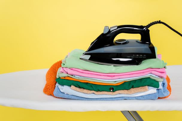 Sarı üzerine izole edilmiş ütü masasına temiz çamaşır ve ütü yığını. - Fotoğraf, Görsel