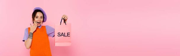 mulher surpreso com venda saco de compras cobrindo boca aberta com a mão isolada em rosa, banner - Foto, Imagem