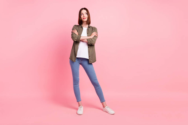 Full size photo of cute brunette hairdo millennial lady crossed arms look empty space wear green shirt jeans isolated on pink color background - Foto, immagini