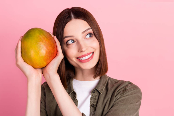 Photo of nice brunette hairdo millennial lady hold mango look empty space wear green shirt isolated on pink color background - Zdjęcie, obraz