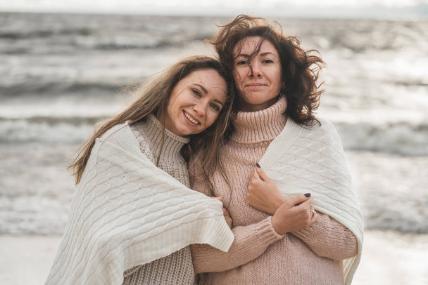 close friends support each other. the sisters walk together by the sea in the fall. the girls wrapped themself in a warm and cozy blanket. sincere love between people.  - Photo, Image