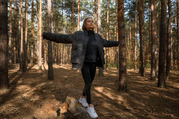 A girl walks on a log in a pine forest in autumn. Girl balancing on a log in the forest - Фото, изображение