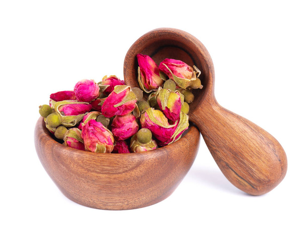 Un mucchio di cime di rose secche di tè in ciotola di legno e cucchiaio, isolate su sfondo bianco. Tè ai fiori di rosa. Percorso di ritaglio. - Foto, immagini