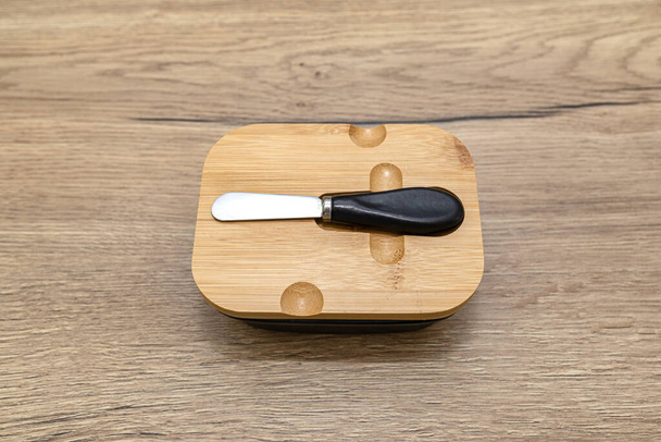 Нож для масла с черной ручкой, лежащий в деревянном чехле на кухонном столе. - Фото, изображение