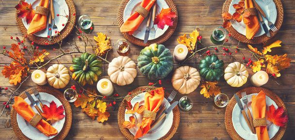 Autumnal decorated table for celebrating Thanksgiving or other family celebration. Festive table setting with plates, glassware, pumpkins, rose hip branches and leaves on wooden table background, top view - Foto, imagen