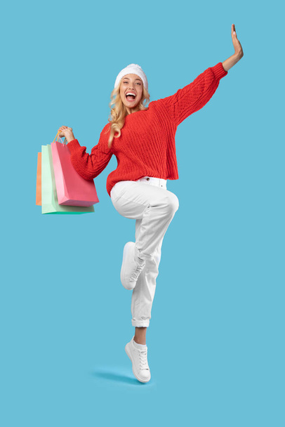 Excited blonde woman jumping with shopping bags at studio - 写真・画像