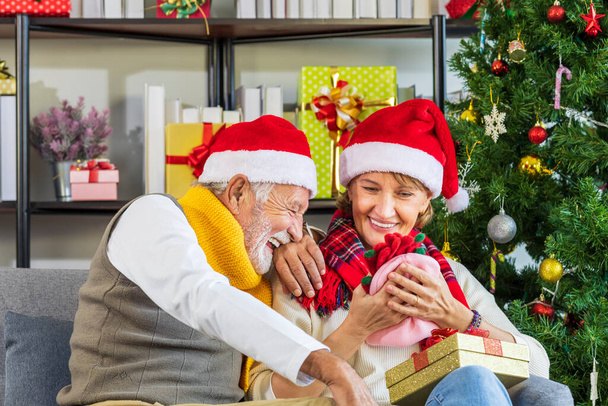 Счастливая старшая кавказская пара в шляпе Санты празднуют Рождество вместе и обмениваются подарками в счастье - Фото, изображение