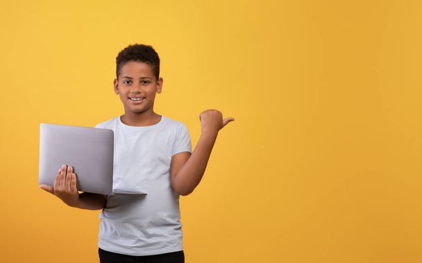 Alegre chico negro con el ordenador portátil apuntando al espacio de copia - Foto, Imagen